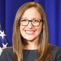Headshot of Marni Goldberg, set against a blue backdrop and an American flag.