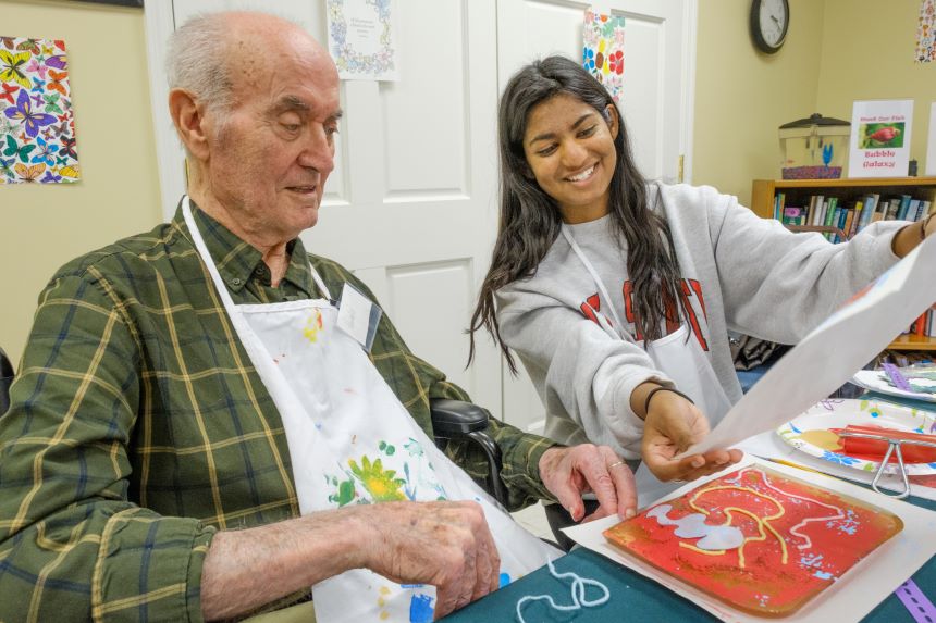 Student working on artwork with an elderly man.