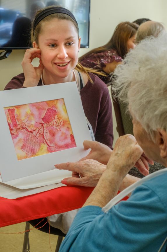 Student with elderly woman holding artwork. 