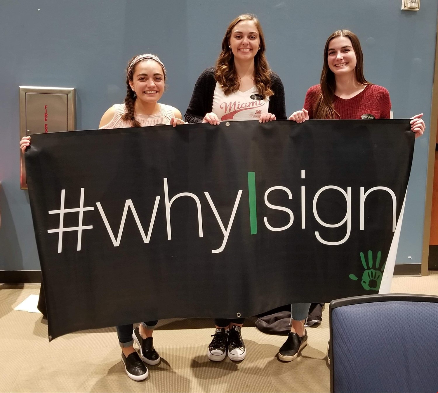 Three students hold a Whi I Sign banner.