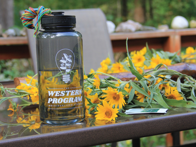 A water bottle with the Western Individualized Studies logo on it with yellow flowers in the background.