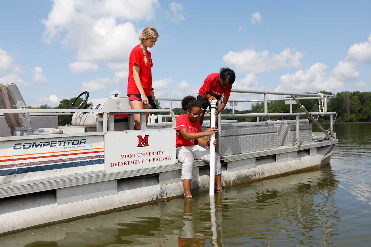 three students gathering water samples from a boat on a lake