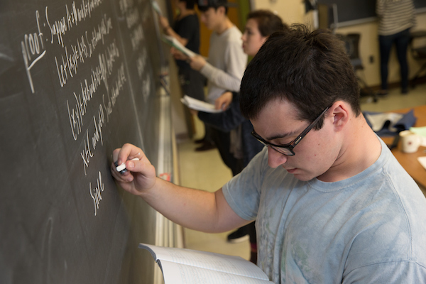 Student doing a math problem at a chalk board