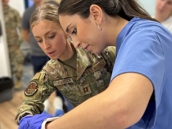 students working on patient, one student in purple scrubs, and the other student in camoflage military uniform