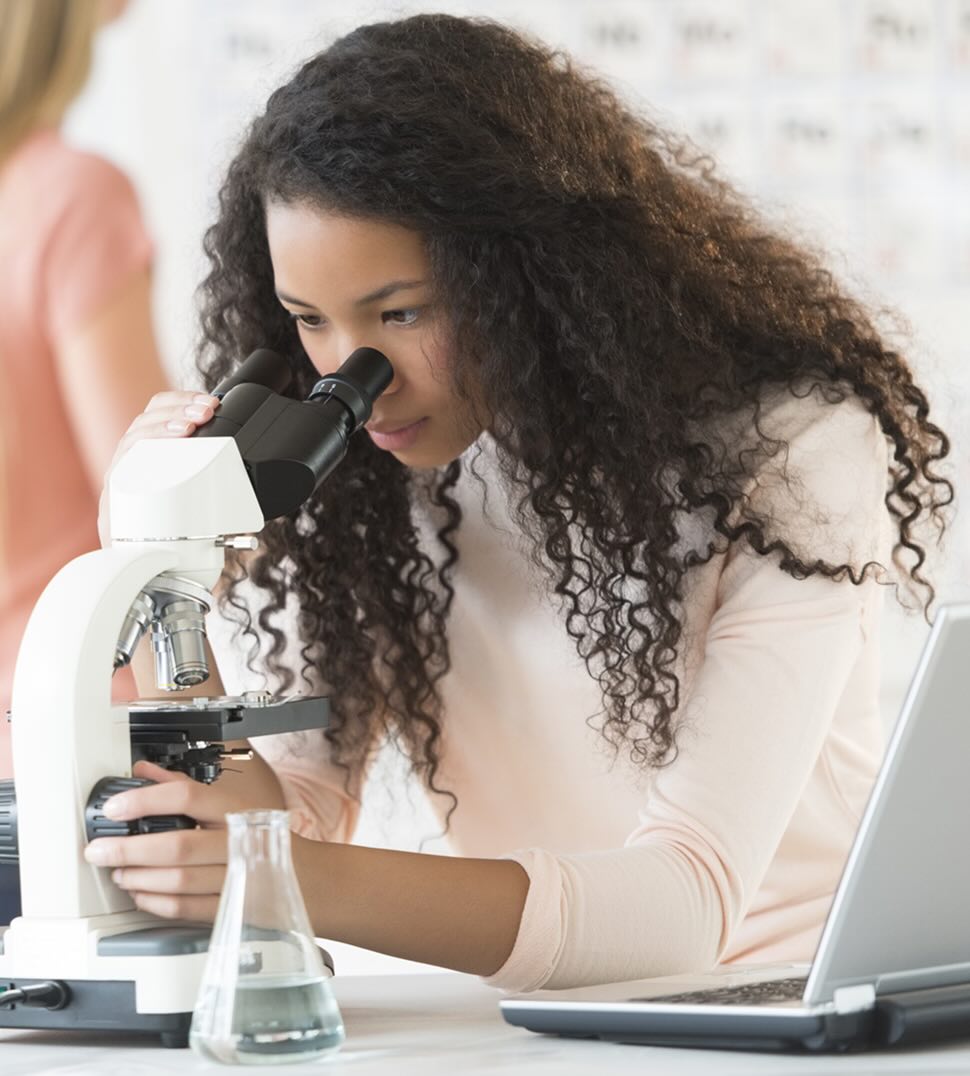 Students in working in a lab one is at a microscope and the other is holding a beaker 