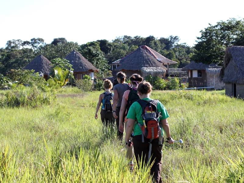 Students walking through grass to a village