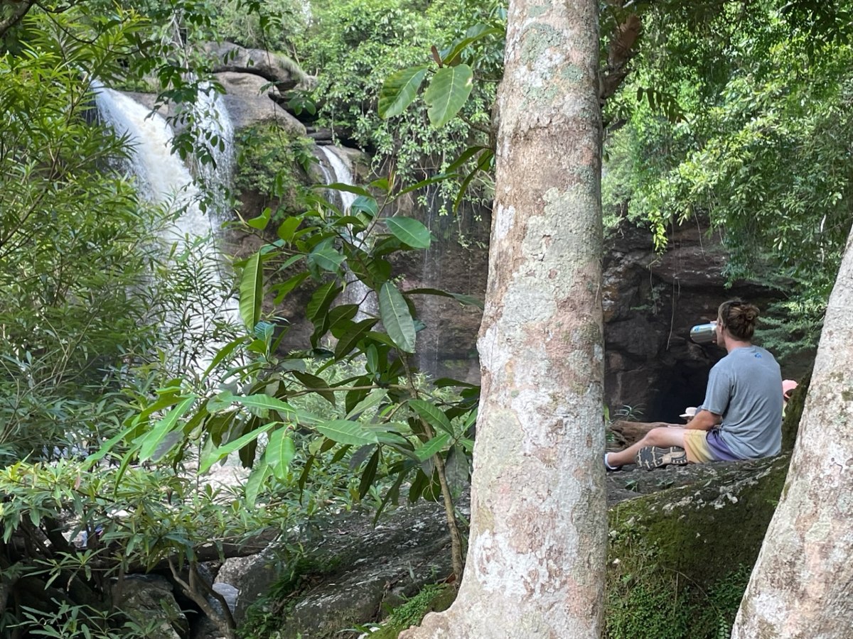 A student sitting by a waterfall drinking some water.
