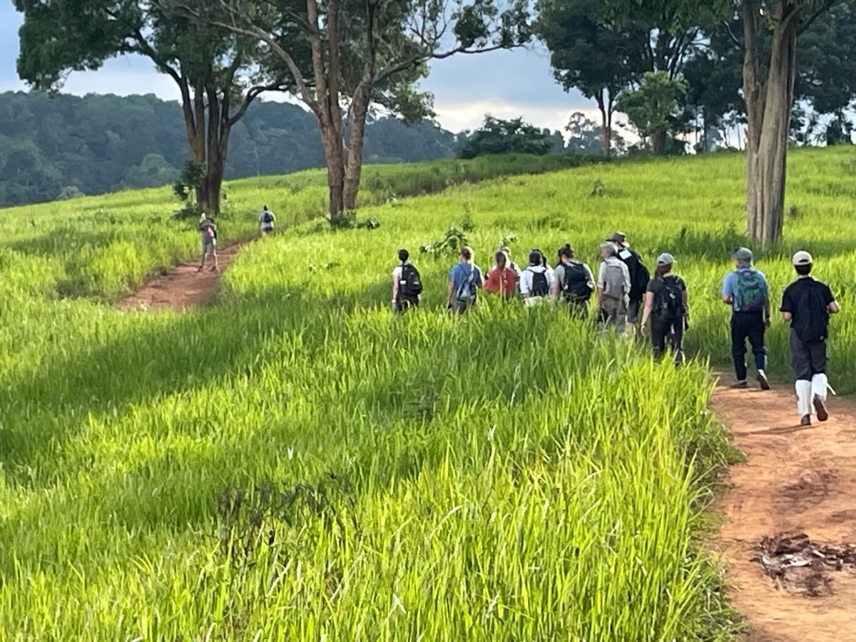 Students walking through a grass field on a dirt path.