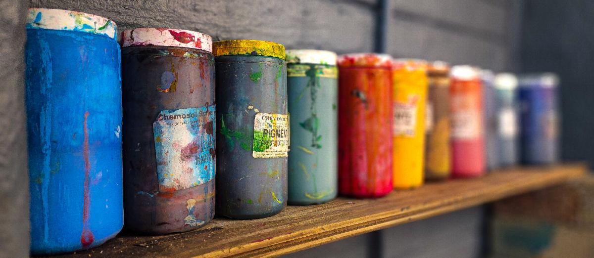 A rainbow of paints sitting on a shelf.