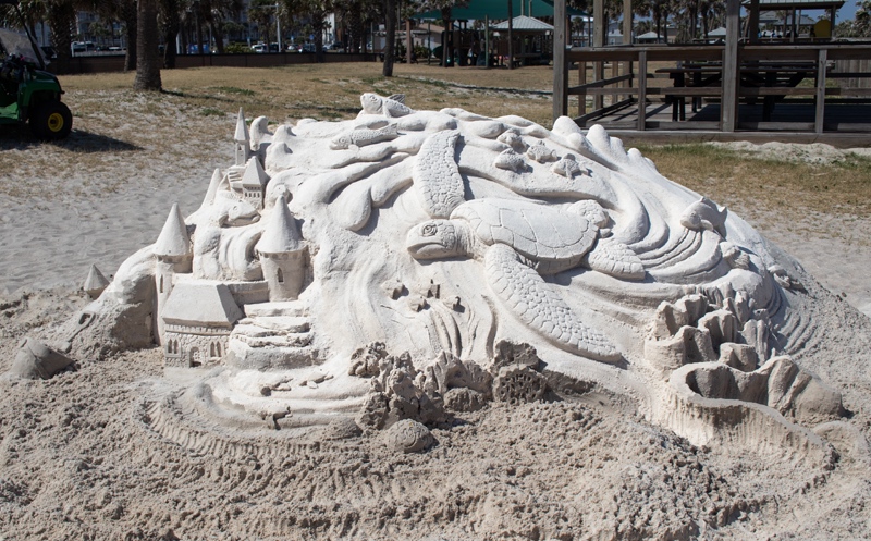 A large sand castle in the sand with a sea turtle included in the design.