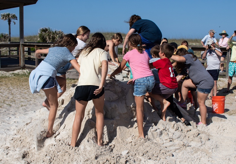 A group of kids climbing on the large sand castle.