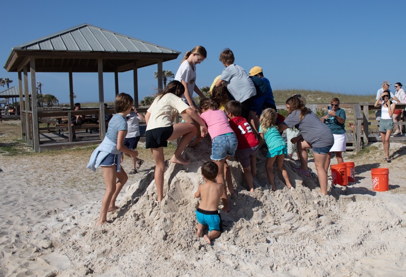 A group of kids climbing on the large sand castle.