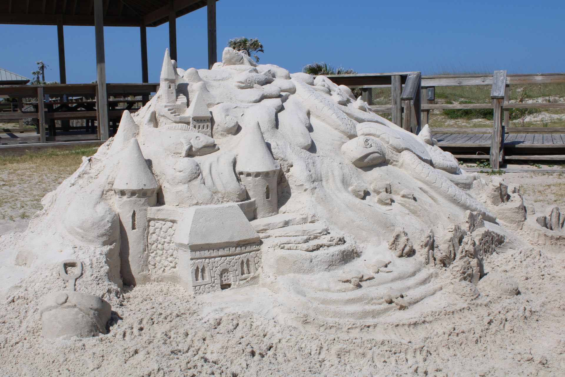A large sand castle in the sand with a sea turtle included in the design.