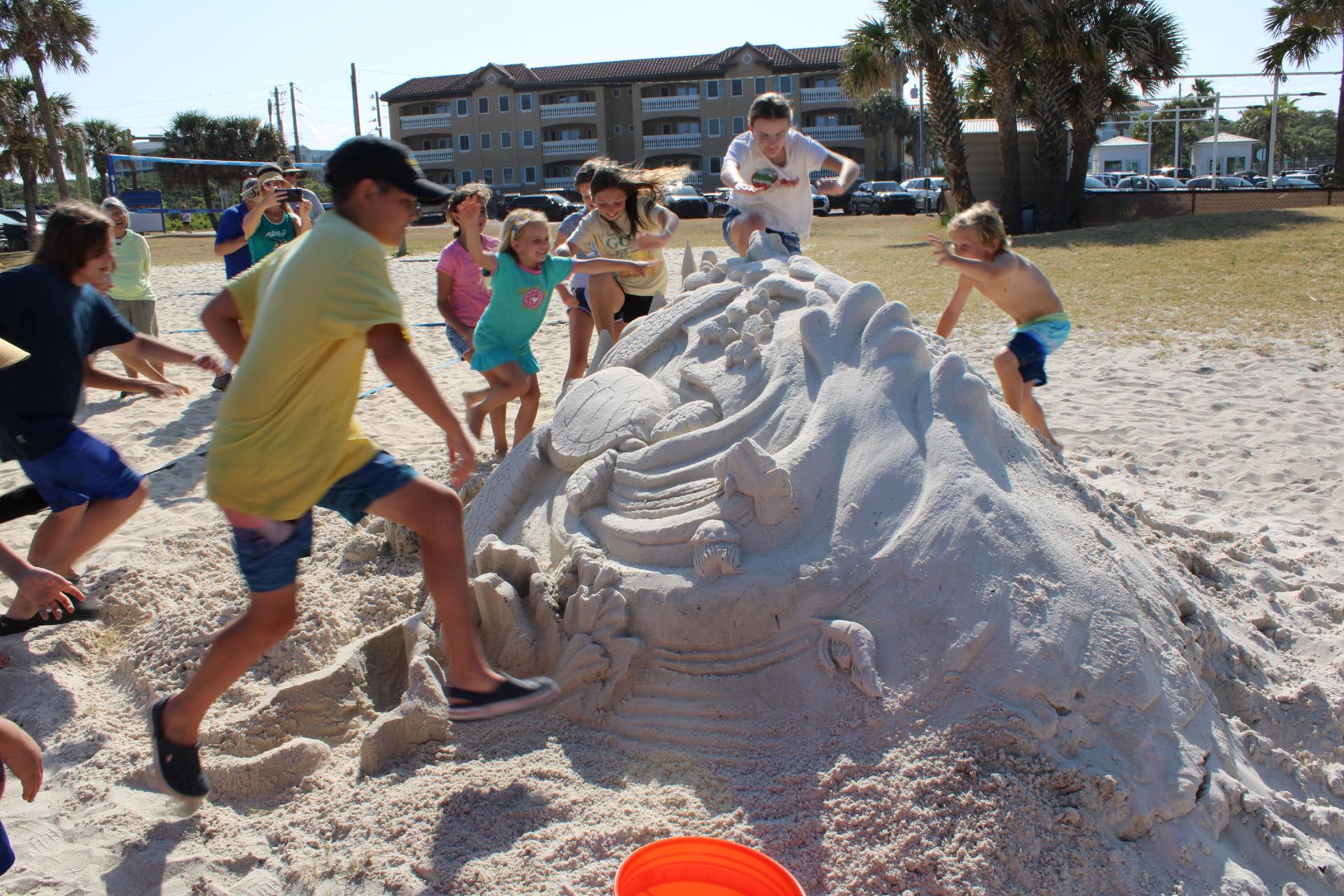 A group of kids climbing on the large sand castle.
