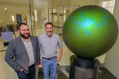 Two men standing next to a large green globe
