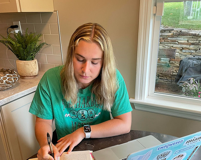 Caroline sitting at the table studying with a book and a laptop