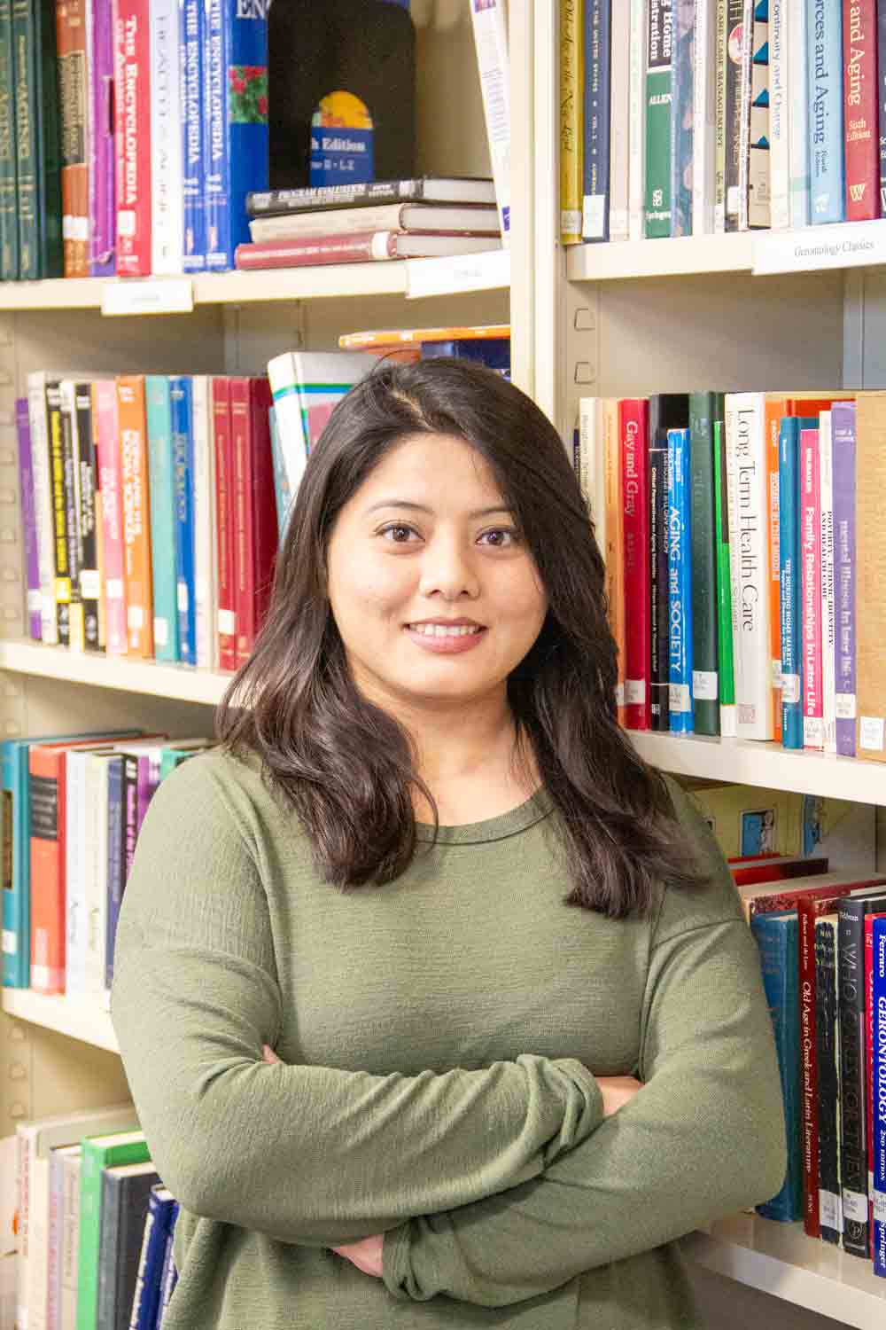 Student standing proudly in front of bookcase. 