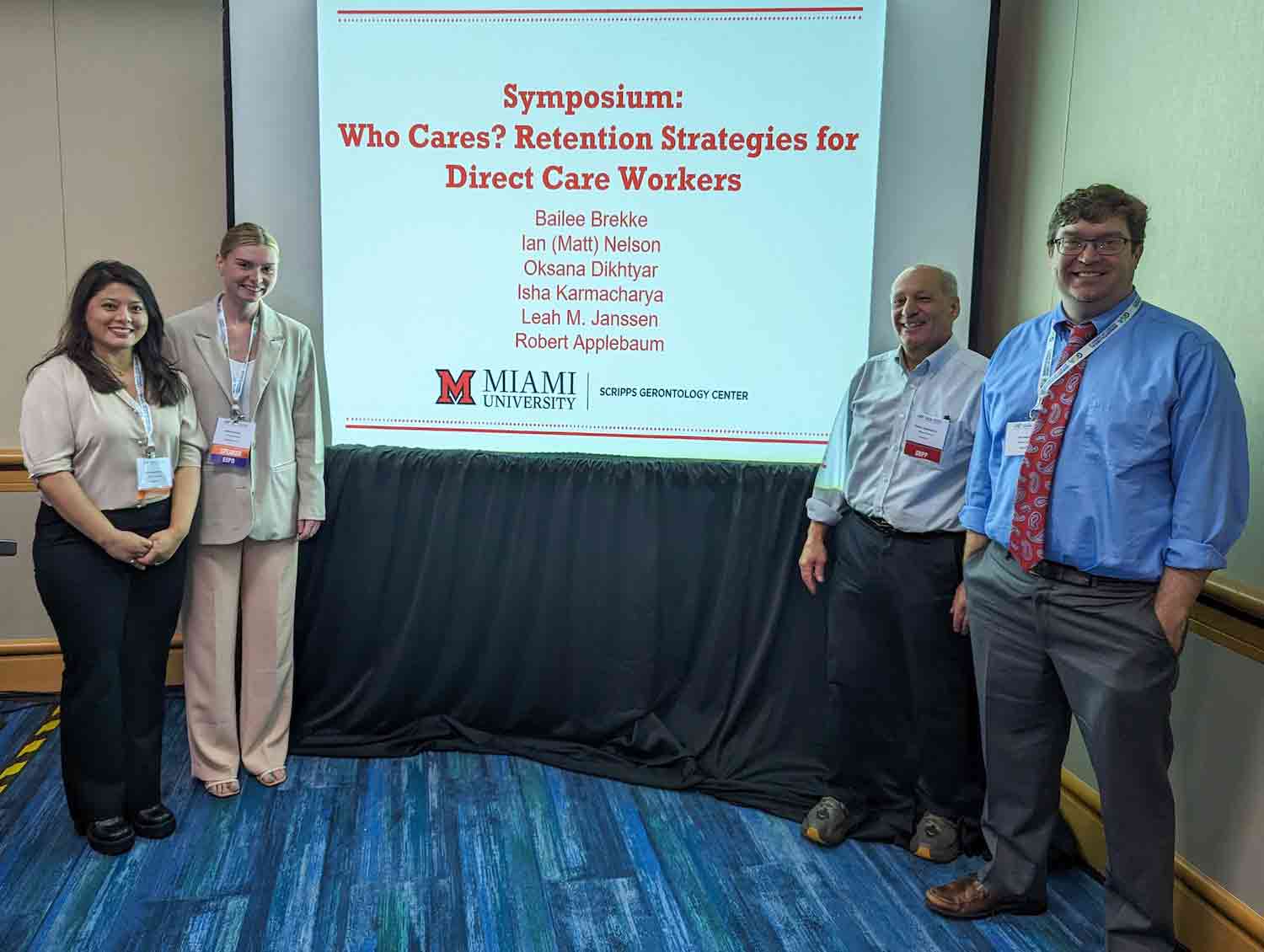 Students and researchers stand next to their powerpoint projection with tile reading, "Who Cares? Retention Strategies for Direct Care Workers"