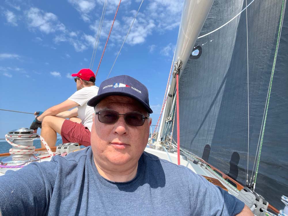 Tony sitting in a sailboats smiling with sunglasses on.