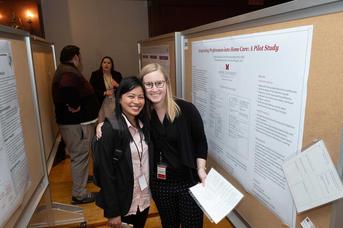 two students hug in front of a gerontology poster.