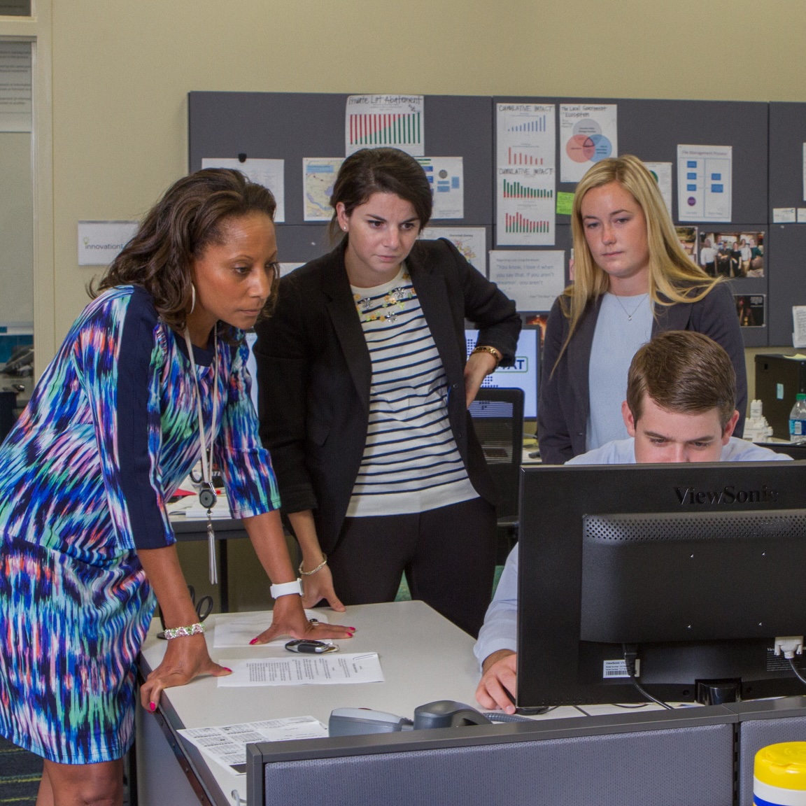 Woman discusses a flight project while gesturing toward a laptop during a meeting in an engineering workspace.