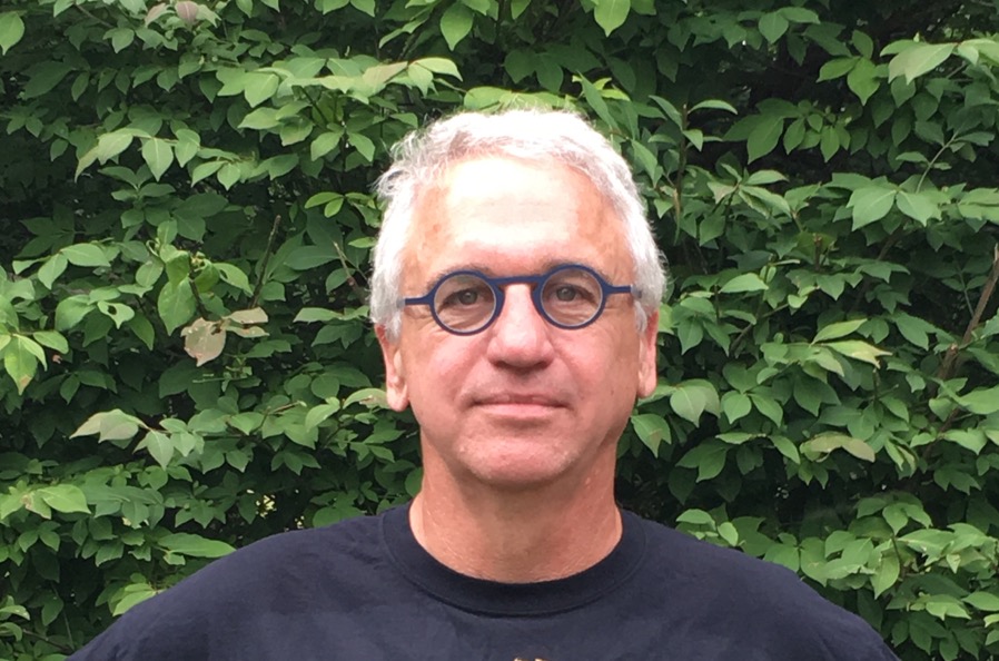 Don Desmett poses in front of green leafy foliage