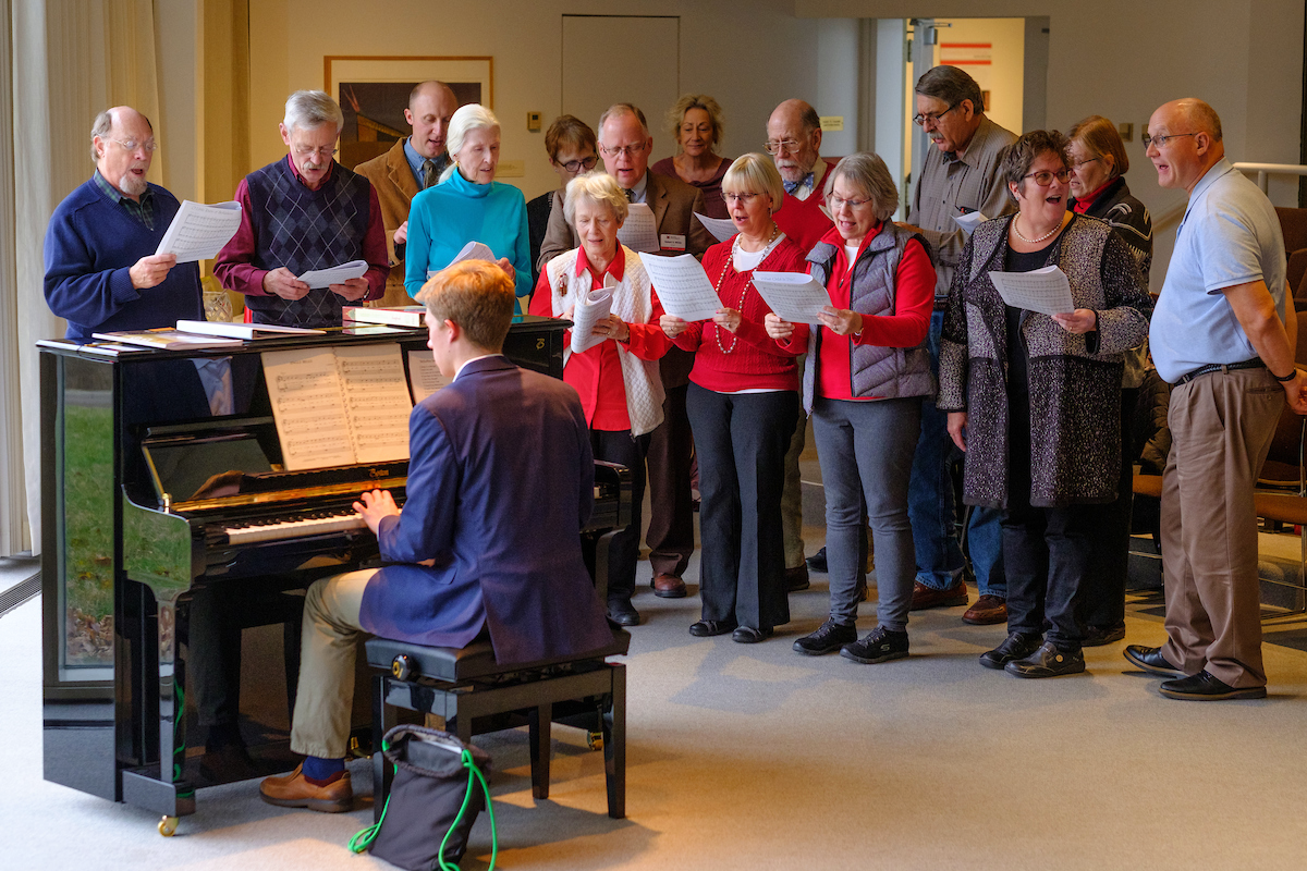 Singers stand near the piano as Jens Bartel plays