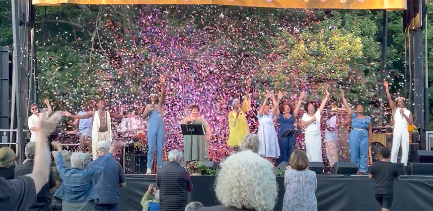 Black performers standing on an outdoor stage while confetti rains down on them
