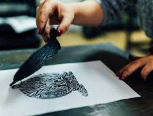 student lifting an inked decorative woodblock creating a leaflike design on paper