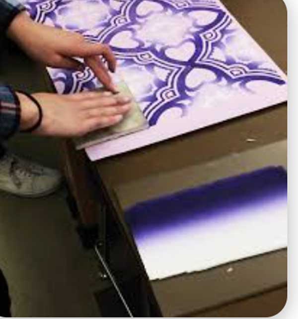 Student pressing a printing block onto paper creating a design