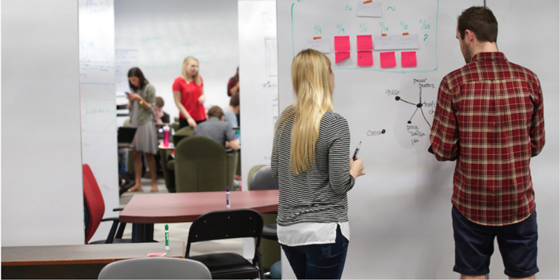 Two students using the whiteboard walls in the AIMS Co-Lab.