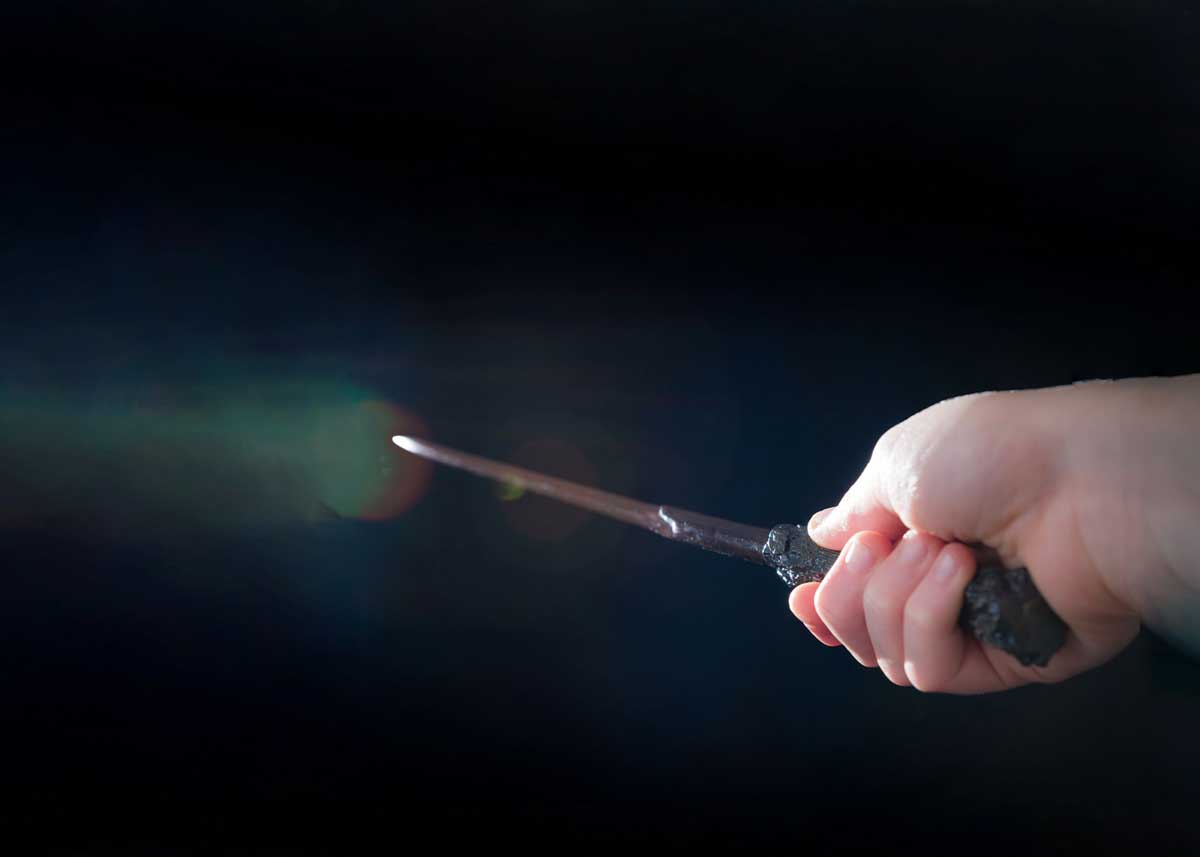 a hand holding a wooden wand with the tip illuminated