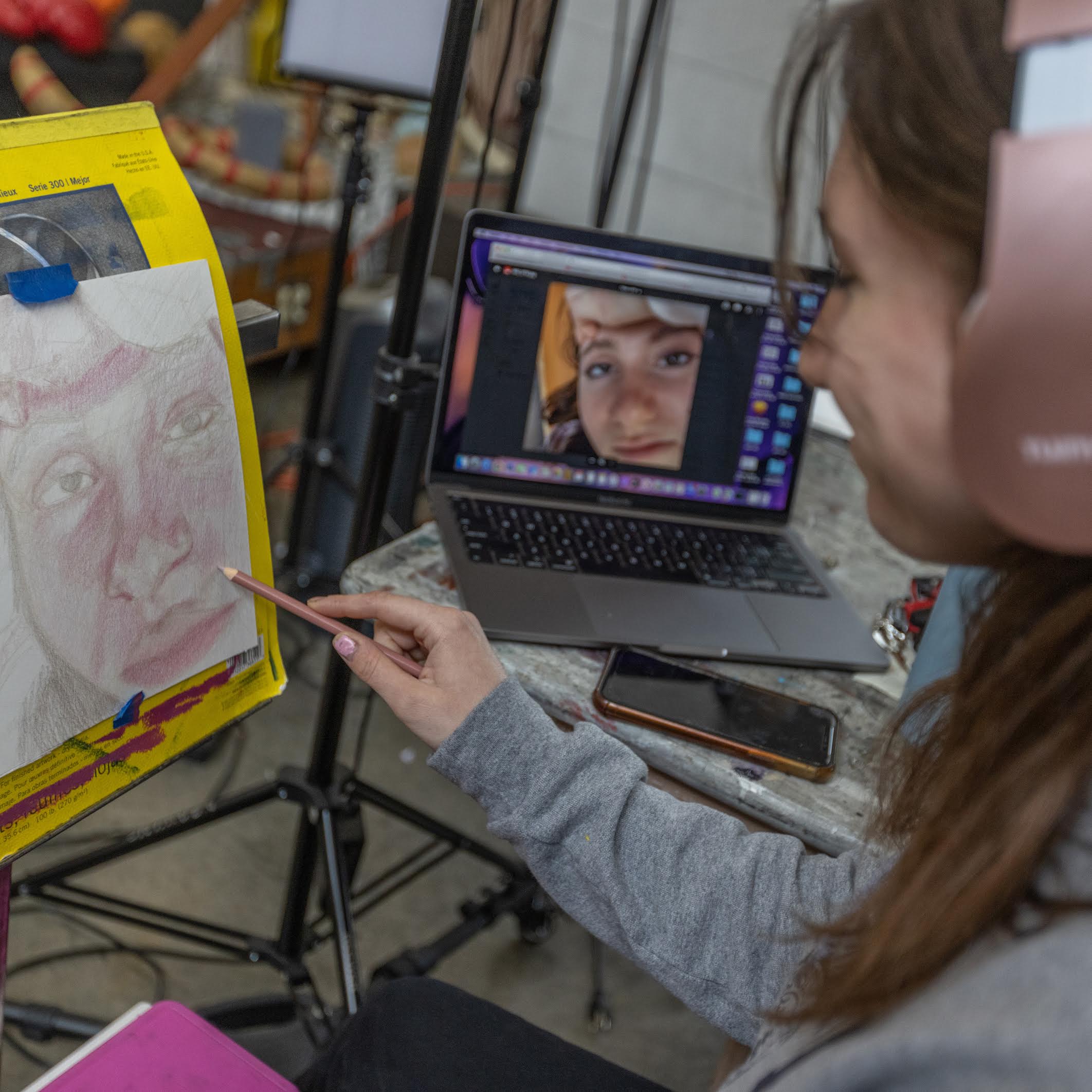 female student wearing headphones drawing on paper on a small easel