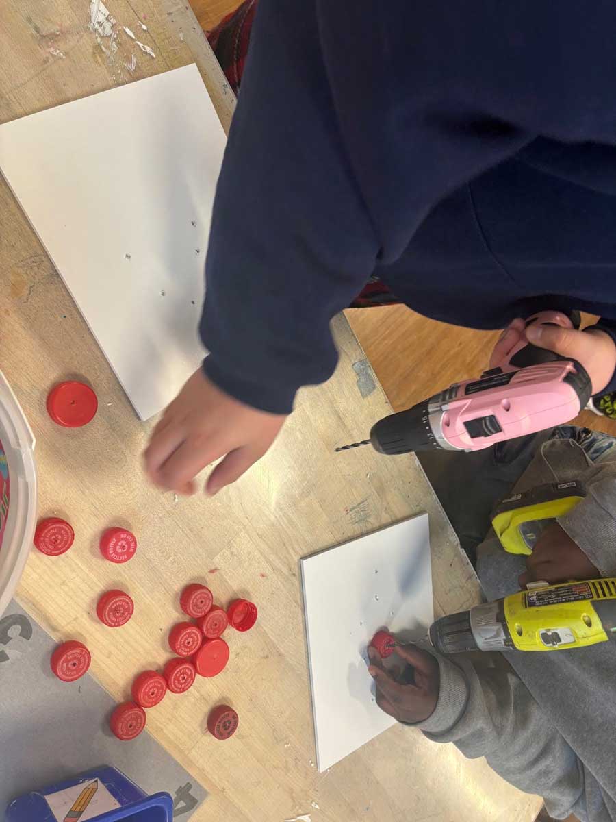 two students drilling holes in the middle of plastic bottle caps