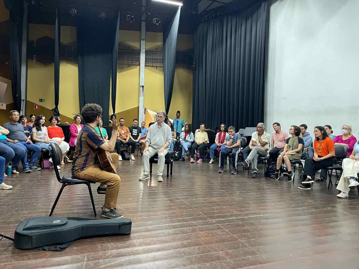 Students surround an instructor in a semicircle who is demonstrating guitar techniques