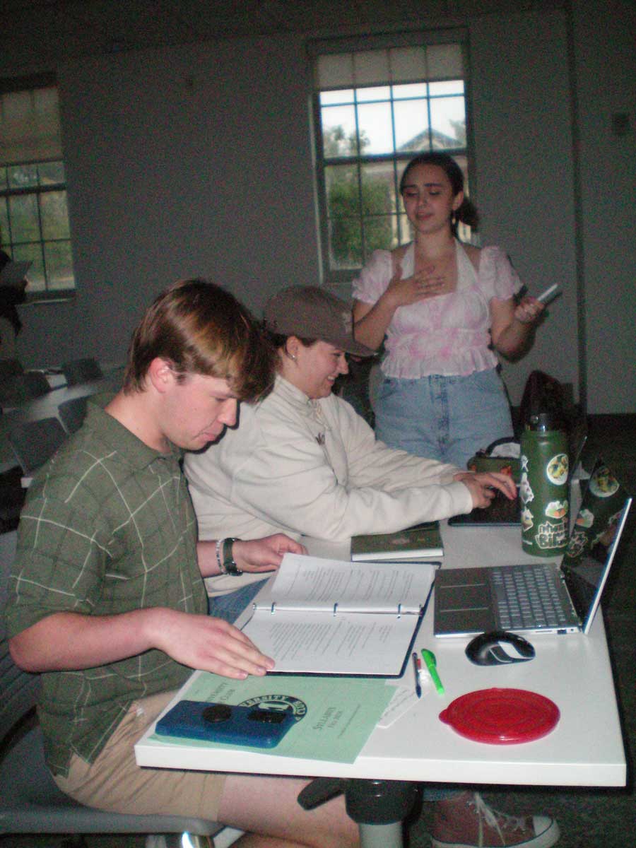 Bradley Beck and Kendra McGuire seated at a table and Mallory Branek standing at the end of the same table