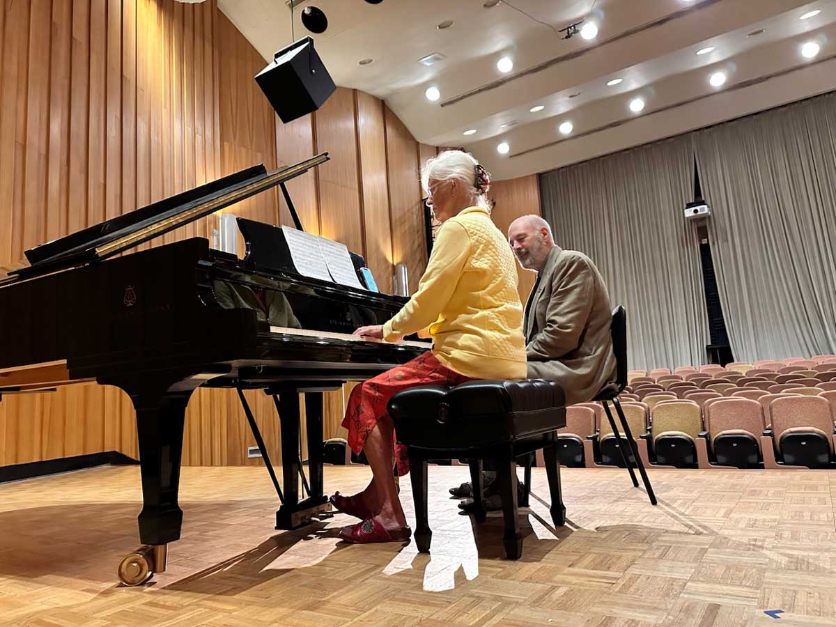 A woman plays a Steinway grand piano on stage at Miami University’s Souers Recital Hall while Alan Fraser, seated beside her, observes during a session of the Alan Fraser Piano Institute.
