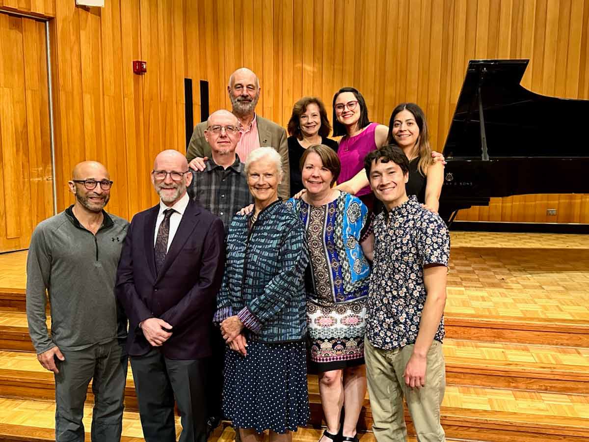 A group of Alan Fraser Piano Institute participants and faculty smile for a group photo in front of a grand piano at Miami University’s Souers Recital Hall following a recital.