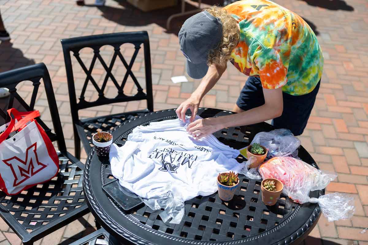 Student tie dyeing a Miami University College of Creative Arts t-shirt on a table.