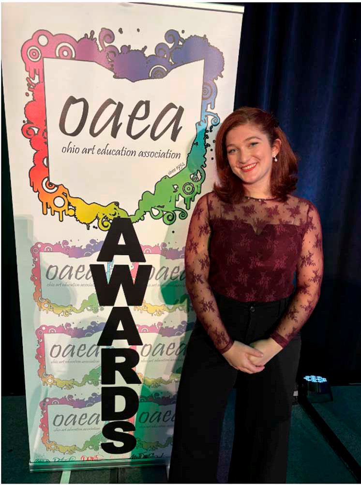 Miami University art education student Ellen Long poses beside the OAEA Awards banner at the 2025 Ohio Art Education Association event.