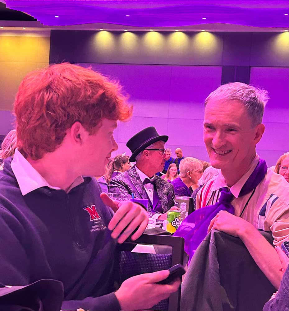 Miami University student Ryan Jeansonne chats with attendees during the 2025 OAEA banquet, with event guests visible in the background.