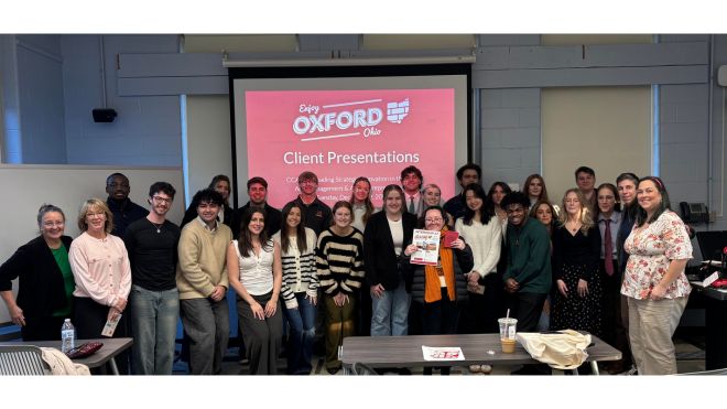 A group of Miami University students and faculty pose in a classroom in front of a screen reading Enjoy Oxford, Ohio – Client Presentations.