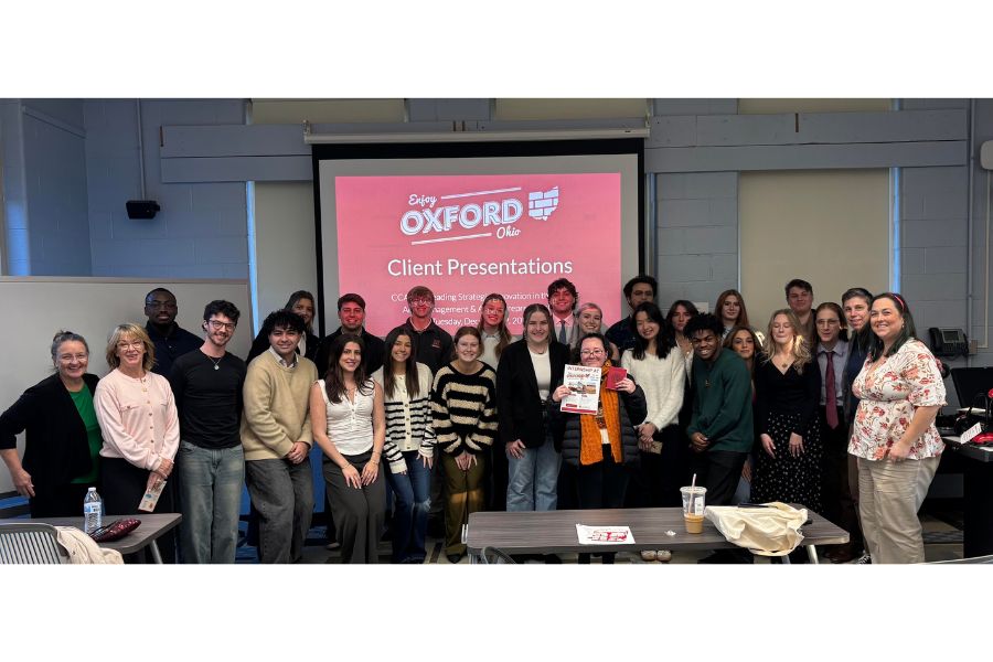 A group of Miami University students and faculty pose in a classroom in front of a screen reading Enjoy Oxford, Ohio – Client Presentations.