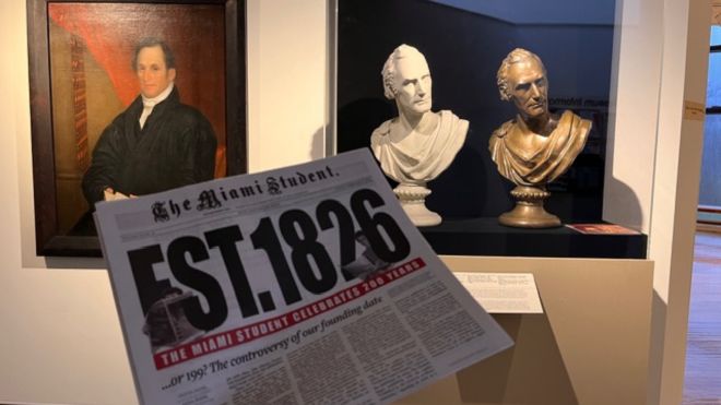 A painting and two bust statues depicting Robert Hamilton Bishop behind a publication of the Miami Student newspaper celebrating its 200th anniversary.