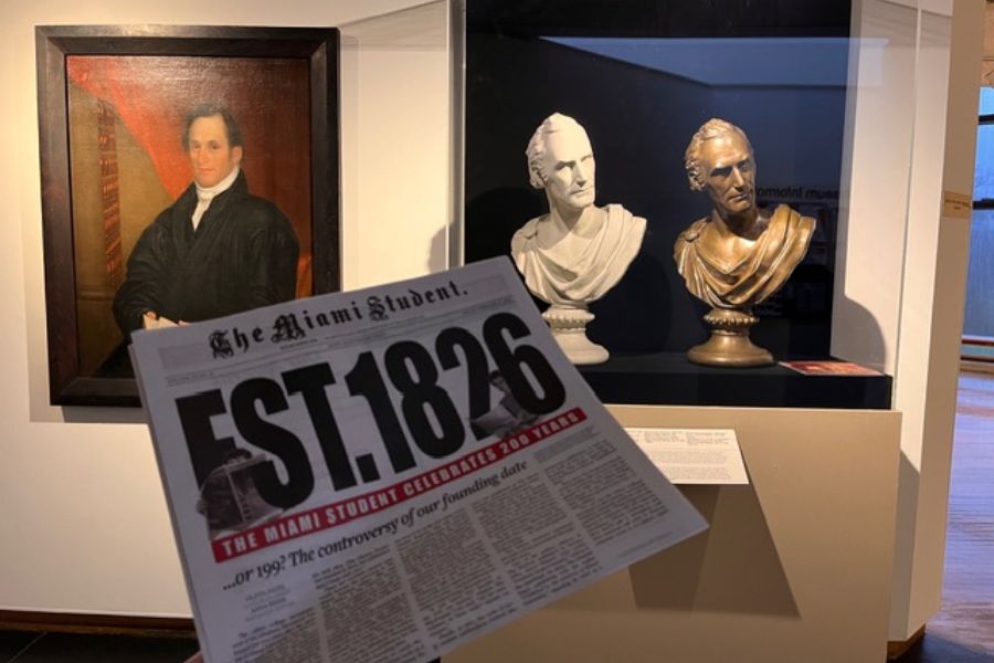 A painting and two bust statues depicting Robert Hamilton Bishop behind a publication of the Miami Student newspaper celebrating its 200th anniversary.