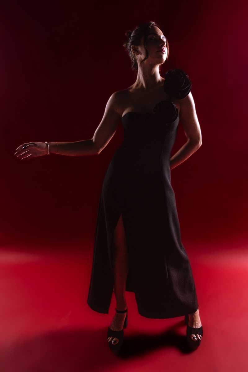 Model in a black asymmetrical dress posing against a red background.