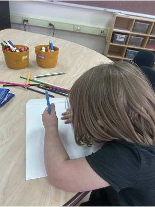 A preschooler creates an illustration for a senior’s story using colored pencils.