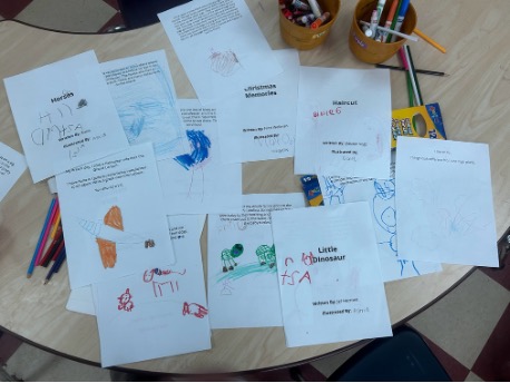 Completed preschool illustrations are spread across a table for the intergenerational art and literacy project.