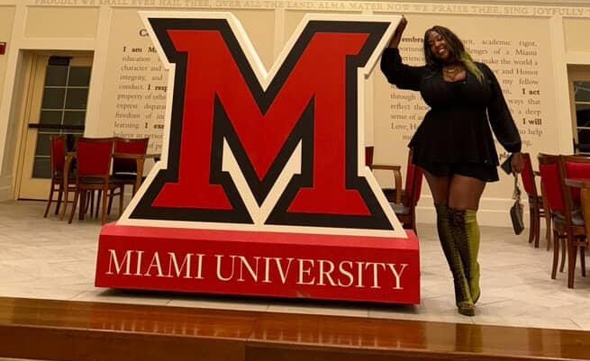 Andrea Bryant posing near large M under chandelier 