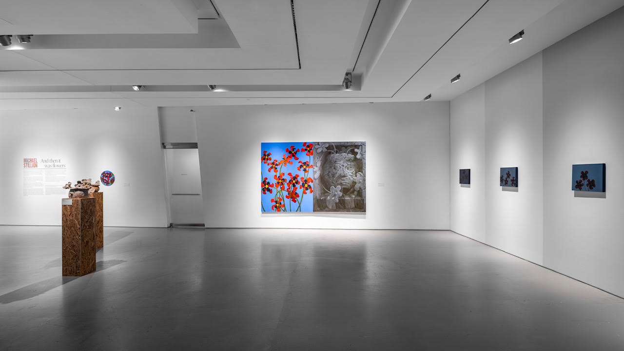 A two-panel painting pairs red flowers on blue with a gray face, with sculptures to the left and smaller floral paintings to the right.